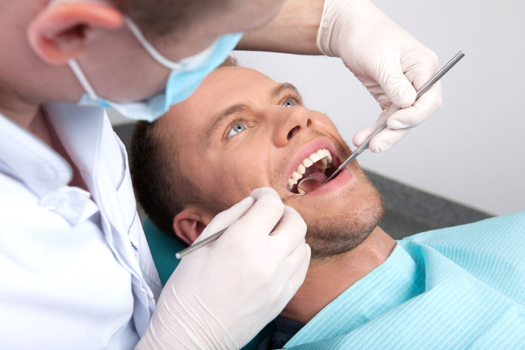Dentist performing teeth cleaning on young male patient
