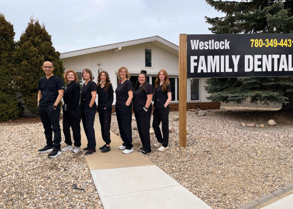 Full team at Westlock Family Dental standing together in front of the clinic entrance sign in Westlock, Alberta