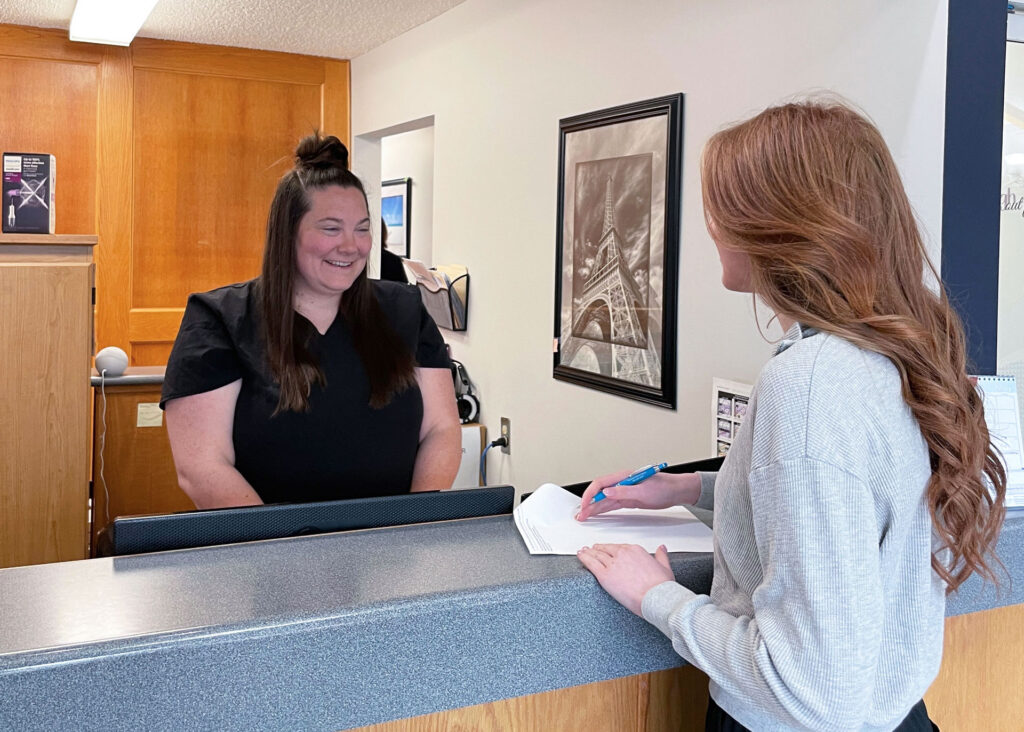 Westlock Family Dental receptionist smiling while assisting a client at the front desk in Westlock, Alberta