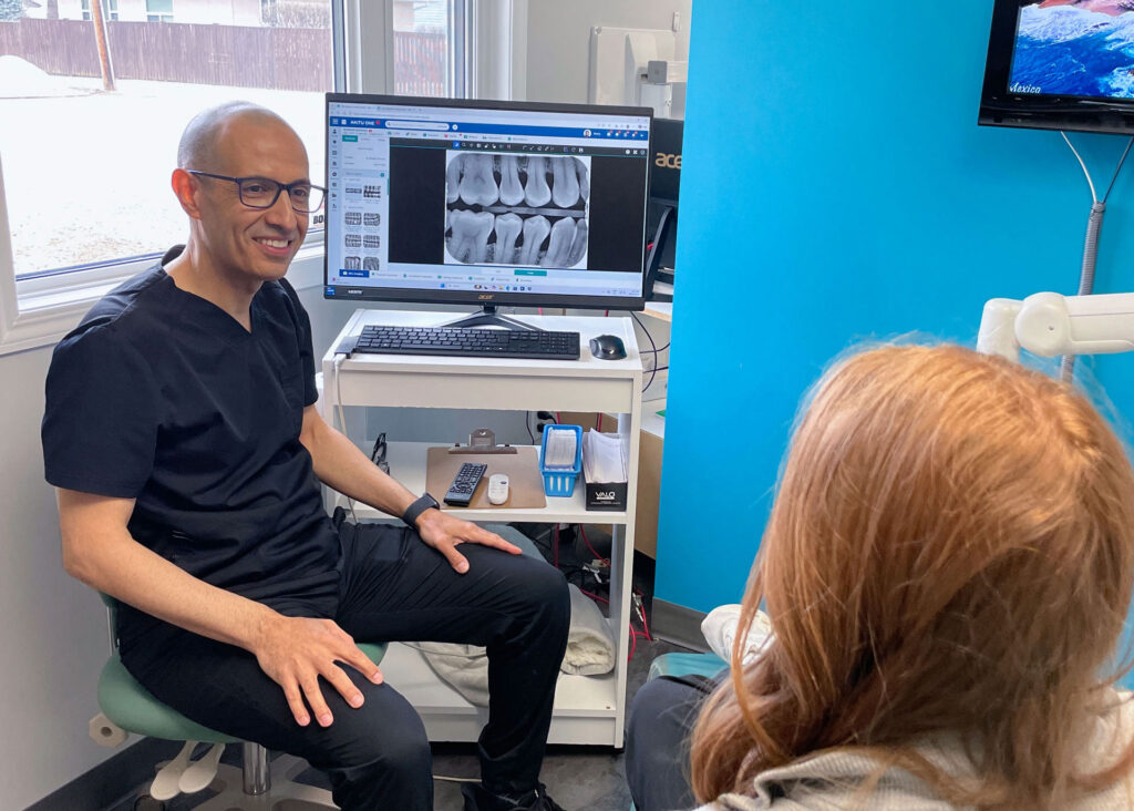 Dr. Mukhtar Alnoaimi at Westlock Family Dental sitting with a patient in a dental clinical room in Westlock, Alberta